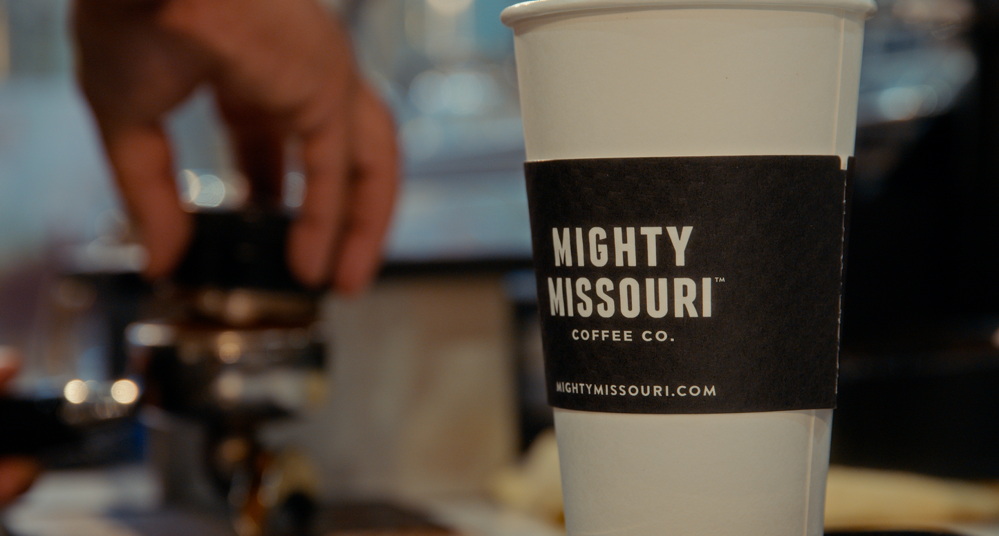 Barista levels fresh roasted espresso in the portafilter. Mighty Missouri branded coffee cup is seen in foreground.